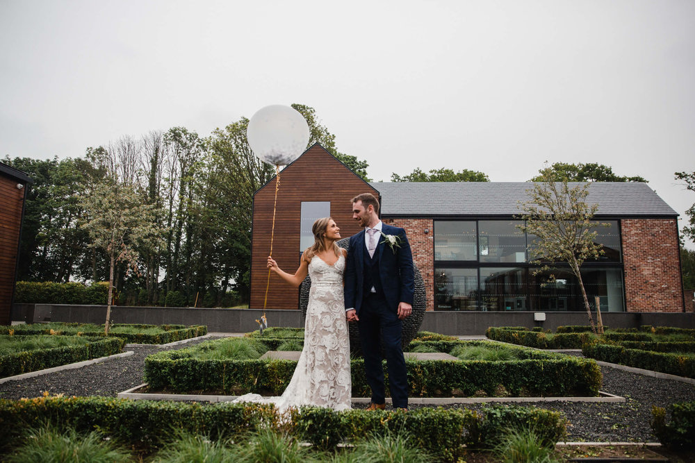 bride holds balloon with groom in gardens at The Colony HQ