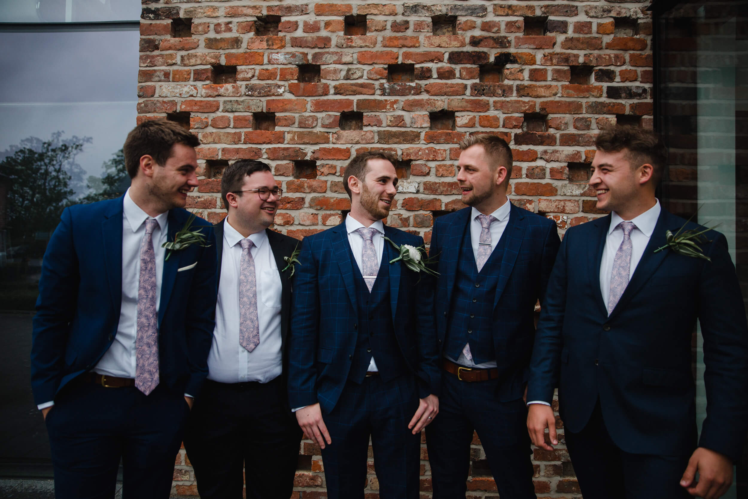 groomsmen in suits pose for group photograph in front of guardhouse