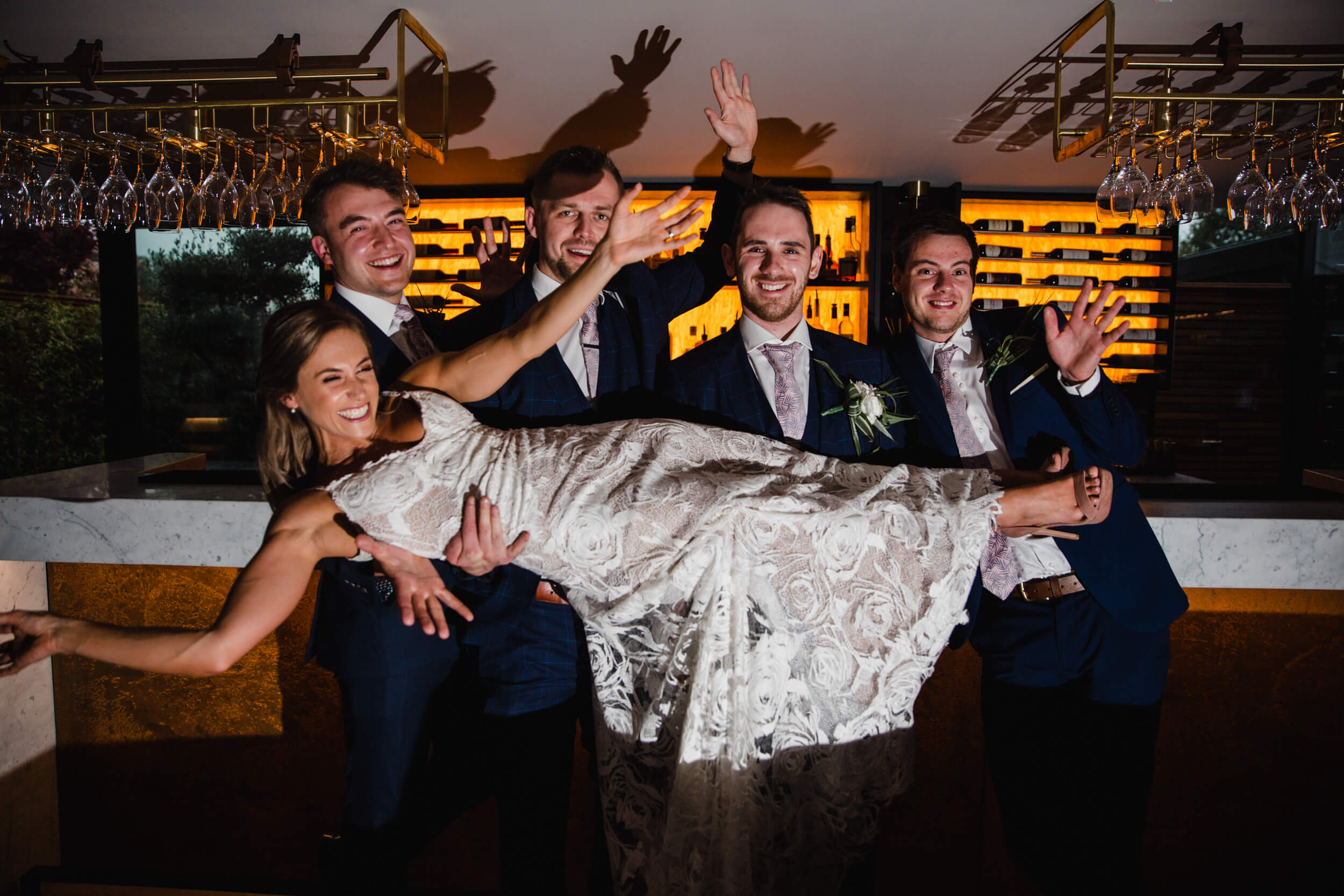 bride and groomsmen group photograph for camera in front of bar post at The Colony HQ