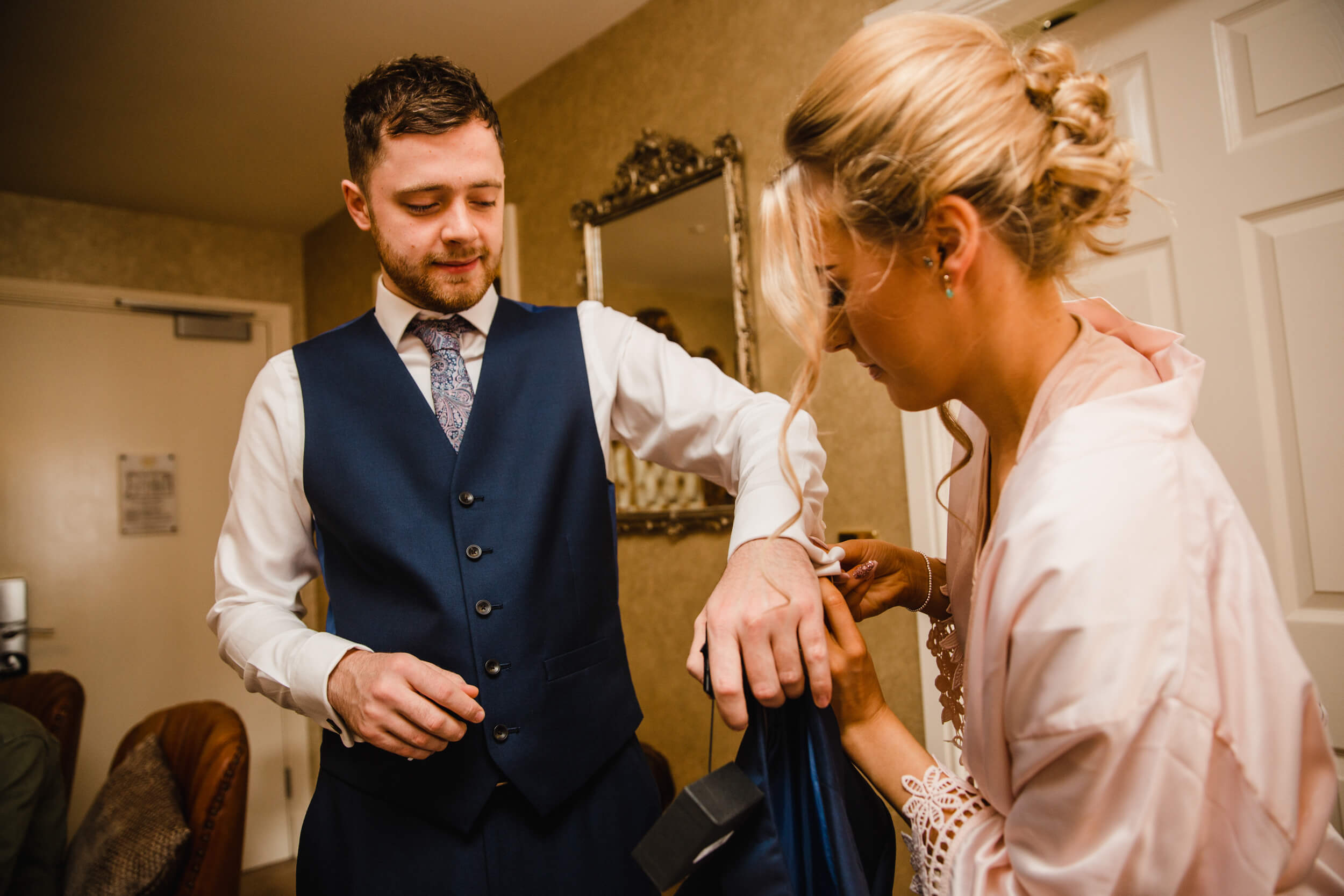 groomsman having suit cufflink attached by maid of honour
