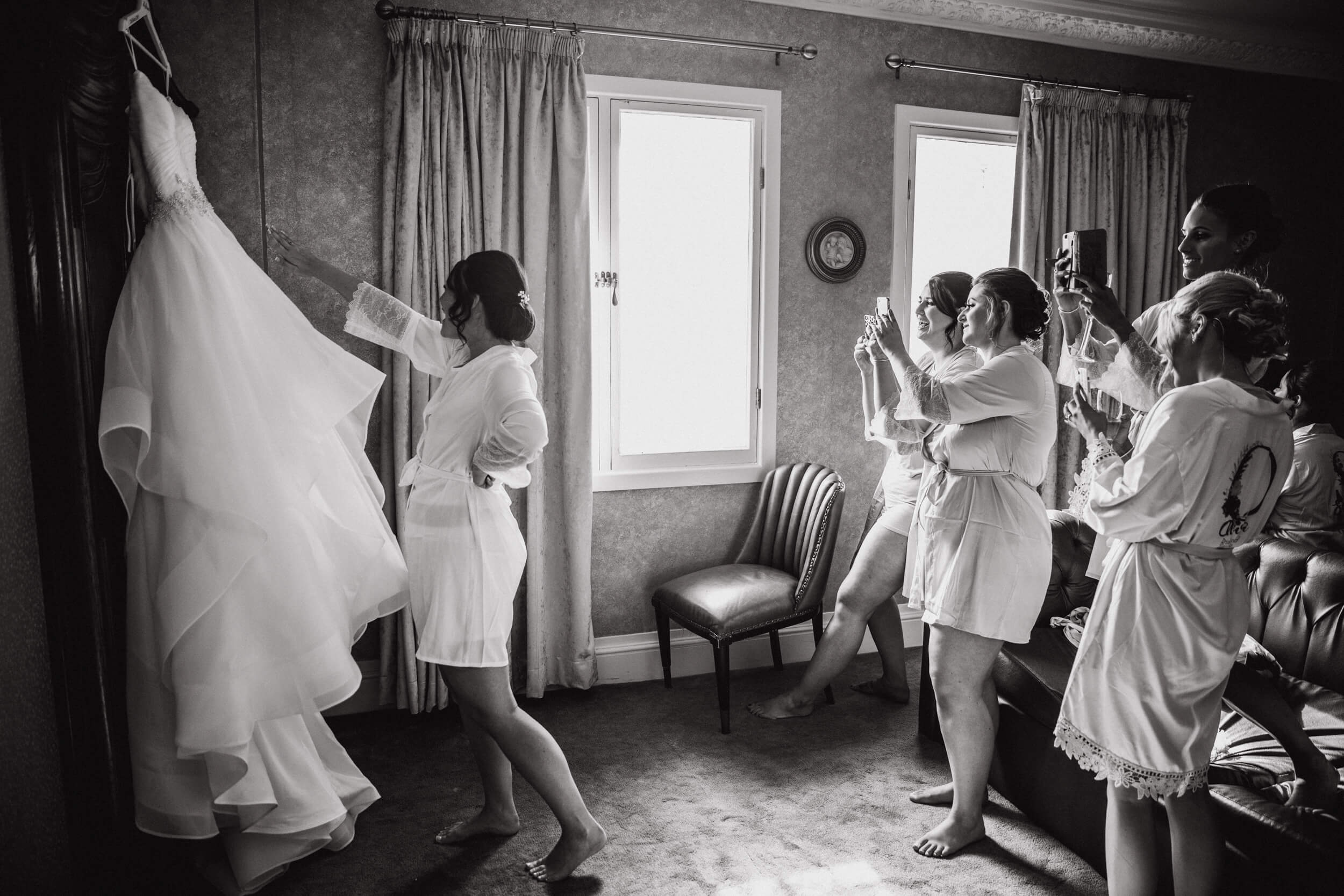 black and white photograph of bride and bridesmaids hanging up wedding dress