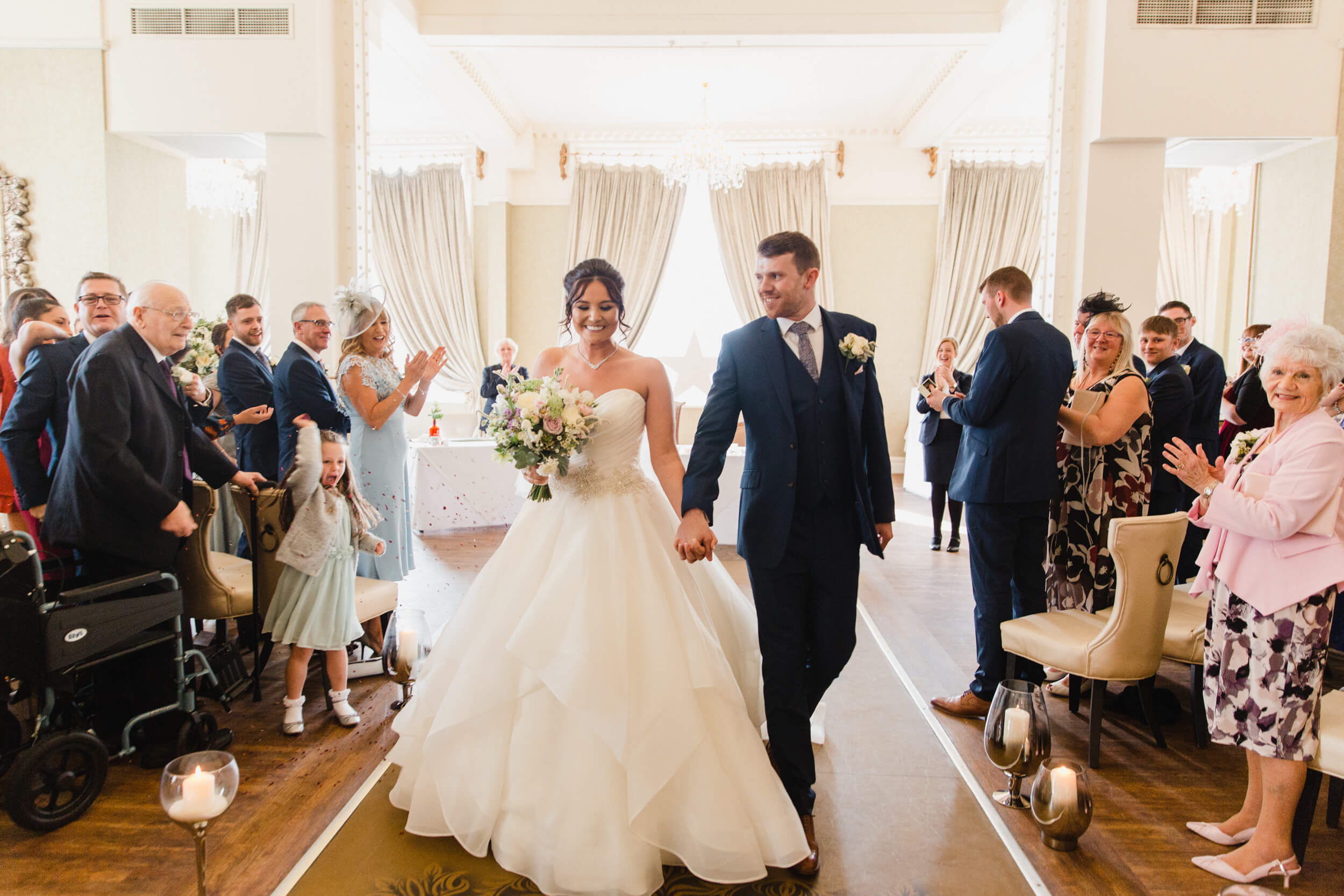 newlyweds holding wedding bouquet being congratulated by friends and family