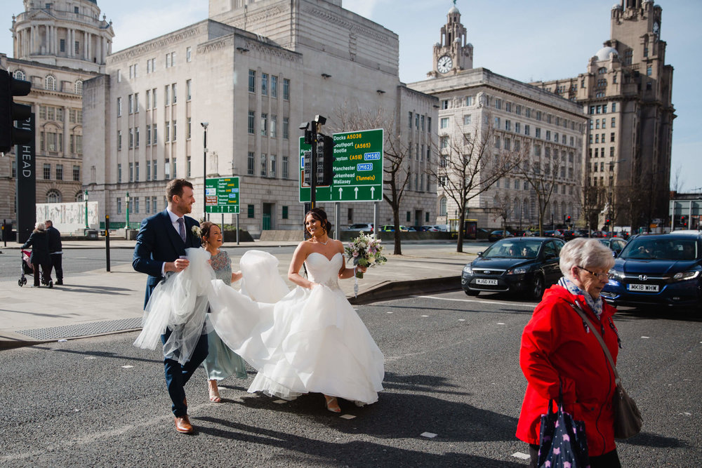 groom and bridesmaid helping carry bride and dress across road at 30 James Street