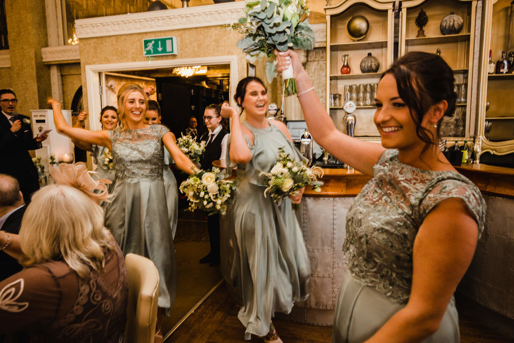 bridesmaids entering wedding breakfast room with dance and waving bouquets in air