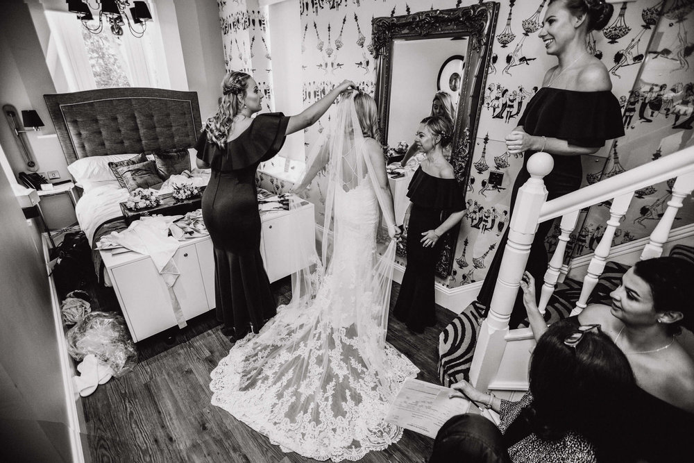 black and white photograph of bride holding veil in mirror with bridesmaids