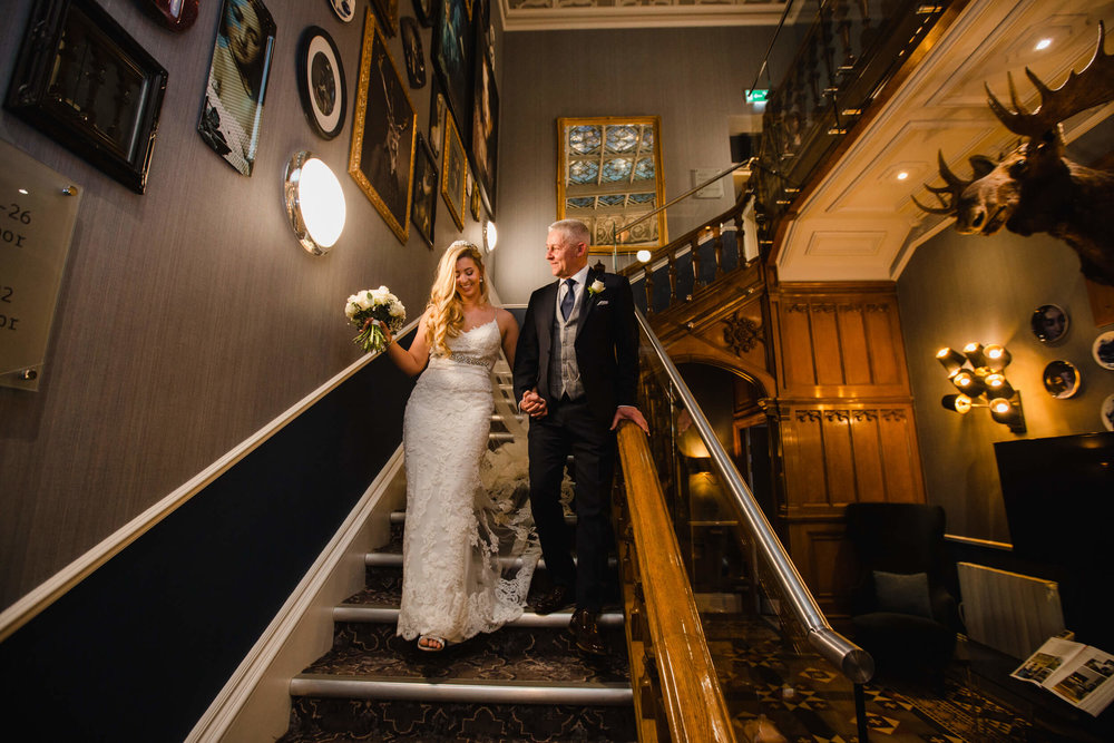 close up of father and bride walking down staircase into hallway