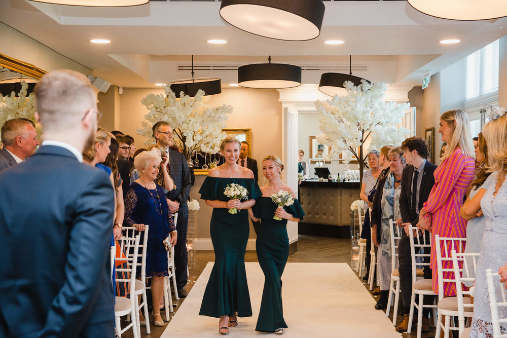 bridesmaids holding bouquets walking down aisle to begin wedding ceremony processional with groom in foreground