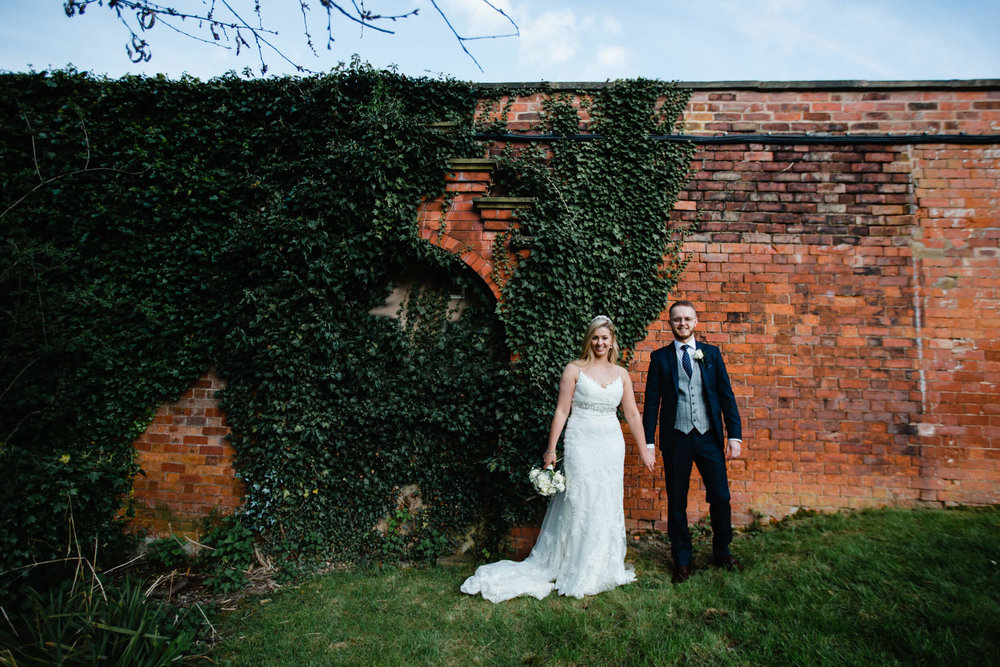 bride and groom holding hands against red brick ballpark wall