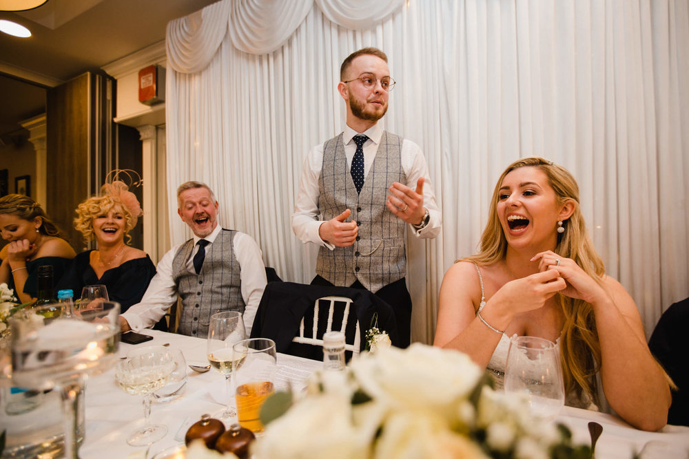 groom delivering speech to wedding party with top table reactions and laughter