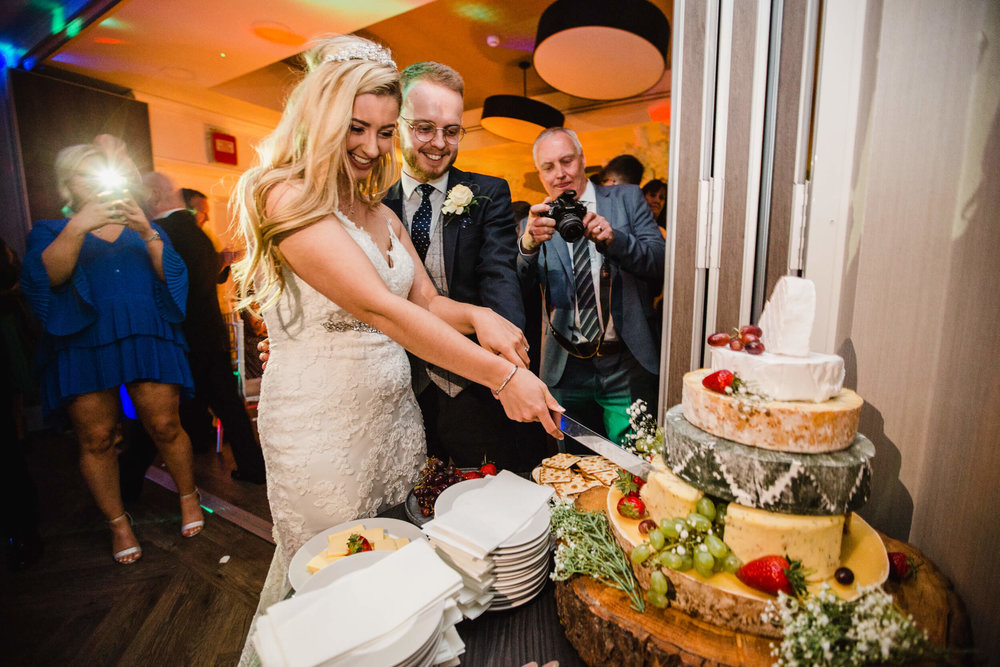 bride and groom cut wedding cake with family and friends