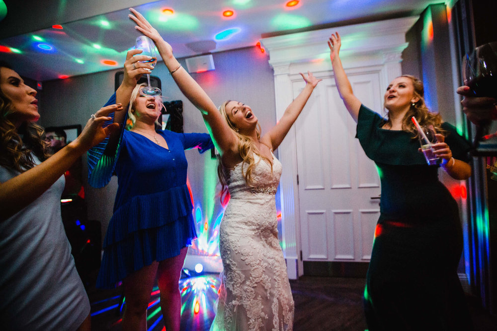 bride and bridal party dancing and holding arms in air at end of night