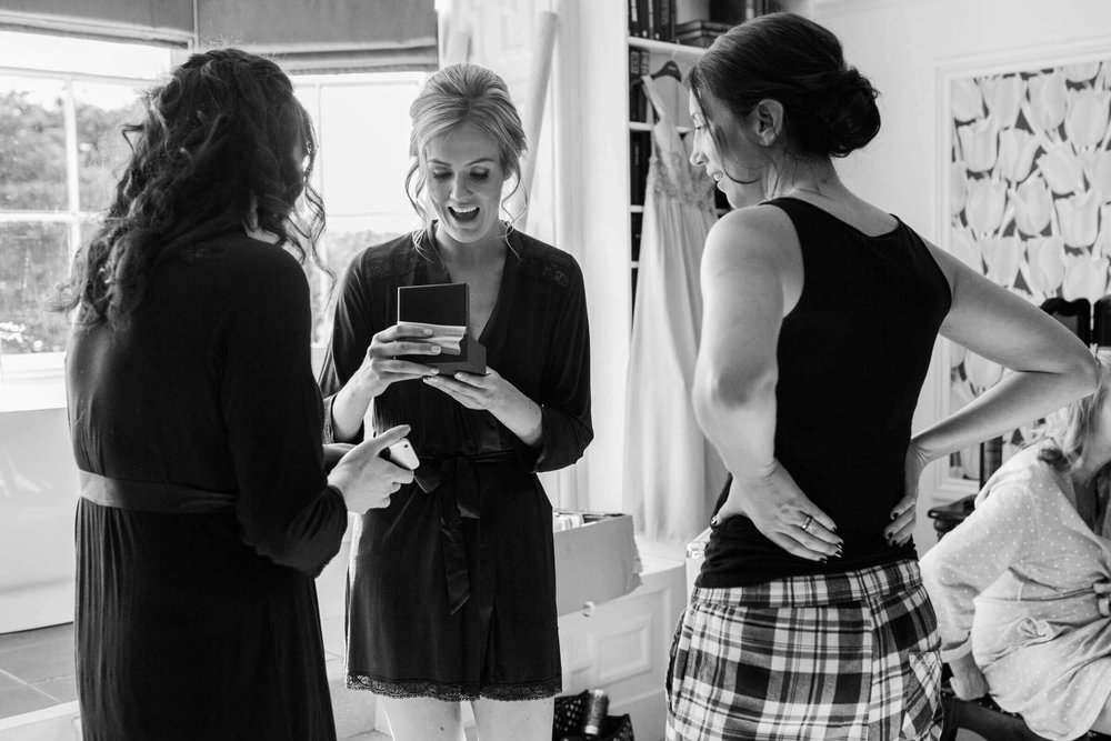 black and white photograph of bride opening wedding gift in front of bridesmaids