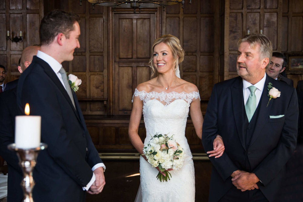 bride walking down aisle linking arms with father being greeted by groom 