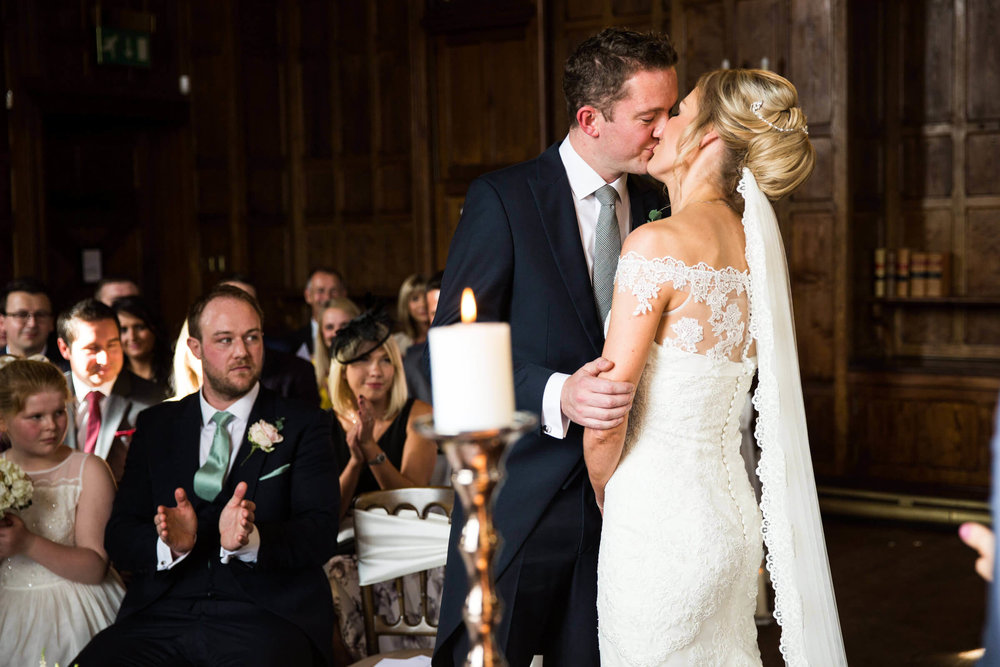 first kiss of bride and groom being applauded by wedding party