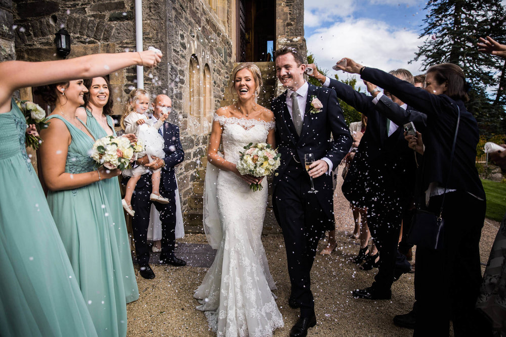 newly married couple enjoying confetti being thrown by bridesmaids and groomsmen