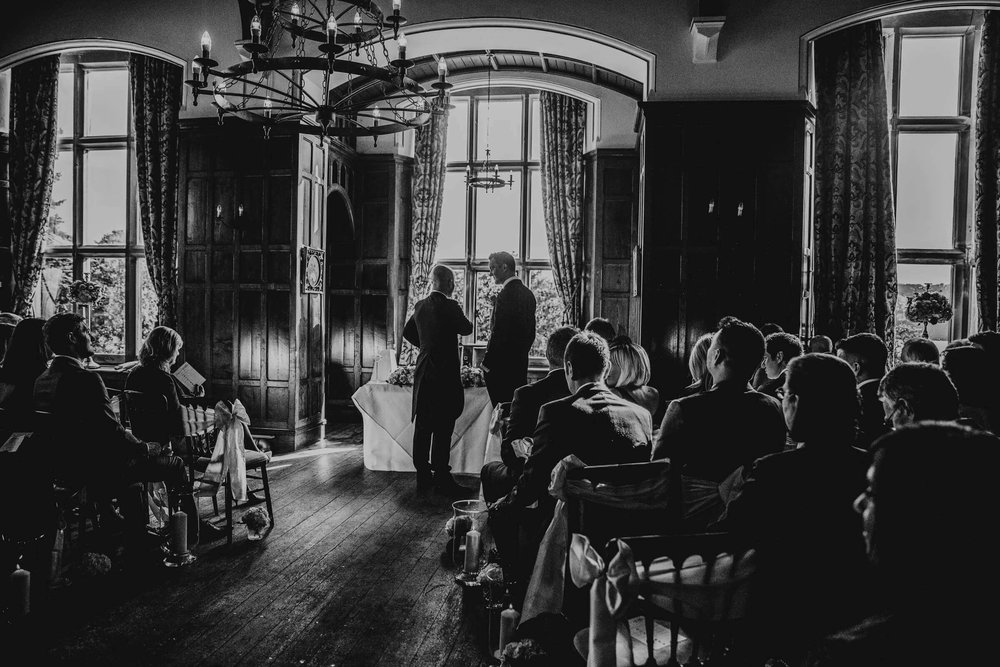 black and white wide angle photograph of groom and best man at top of aisle