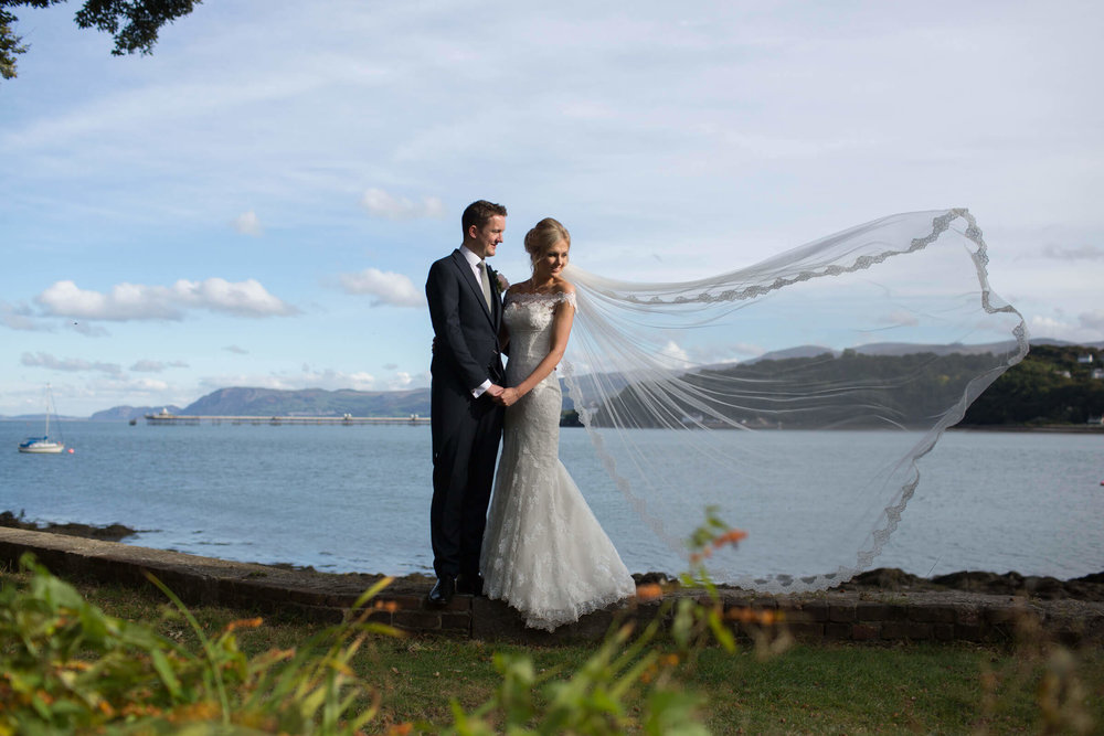 wedding veil portrait photograph of bride and groom posing with seascape backdrop