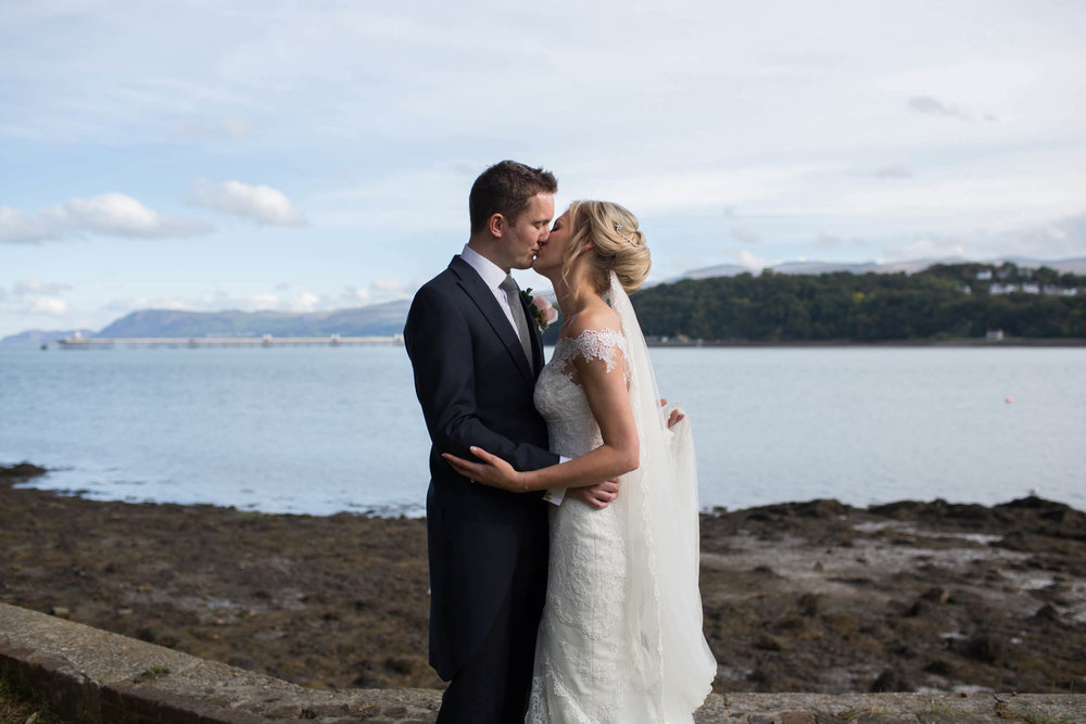 newly wedded couple sharing kiss in front of seascape backdrop