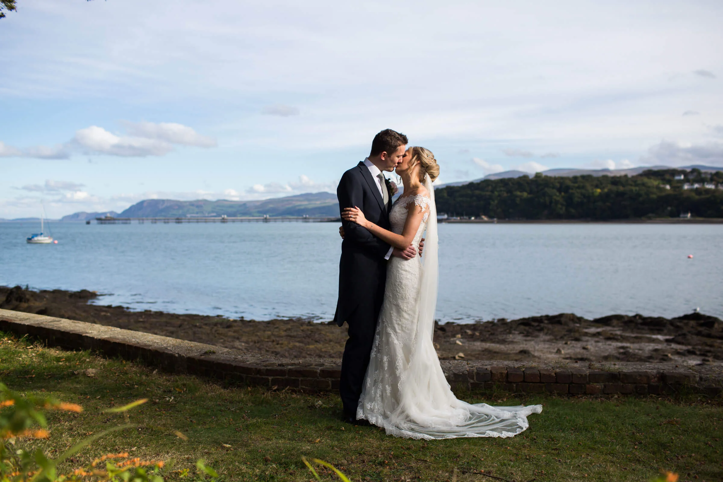 wide angle lens portrait photograph of bride and groom kissing in foreground with seascape backdrop