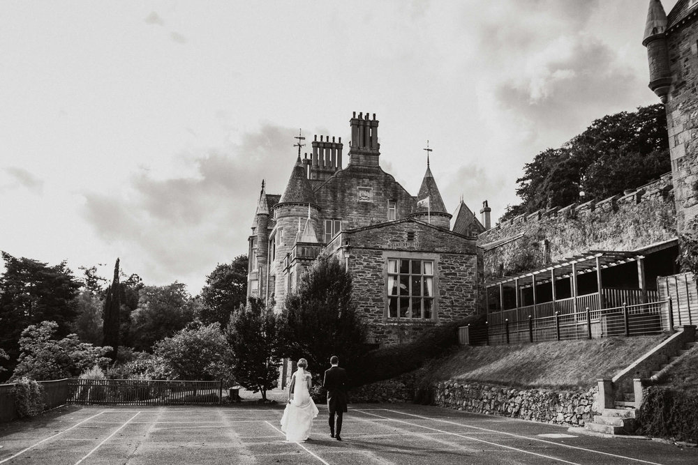 black and white photograph of bride and groom walking away from camera towards chateau rhianfa