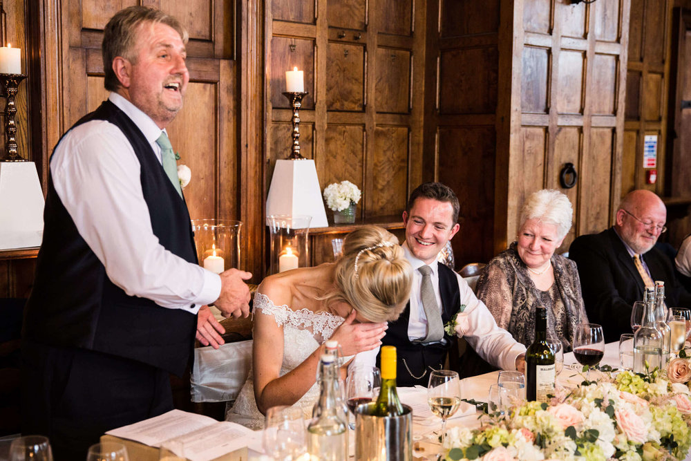 father of bride delivering speech to wedding party with groom and family laughing