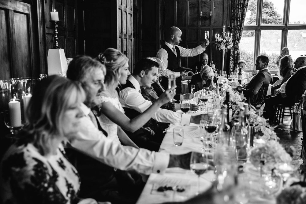 black and white photograph of best man raising a toast to newlywed couple