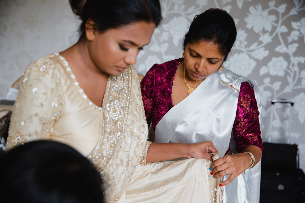 bridesmaid helping bride into wedding gown as part of bridal preparation at delamere manor