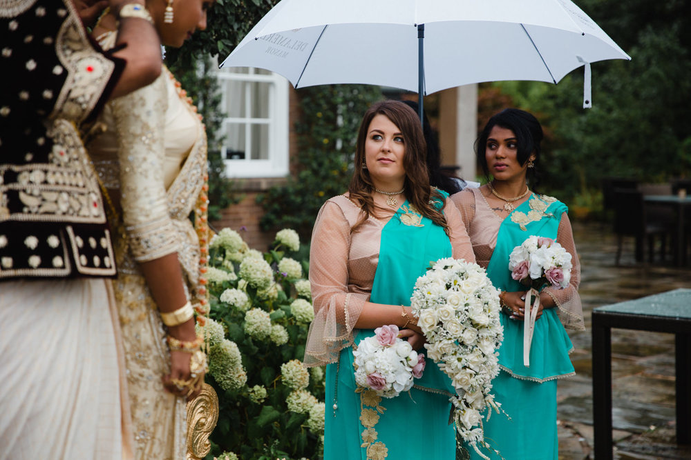 bridesmaids under umbrellas looking at bride during service