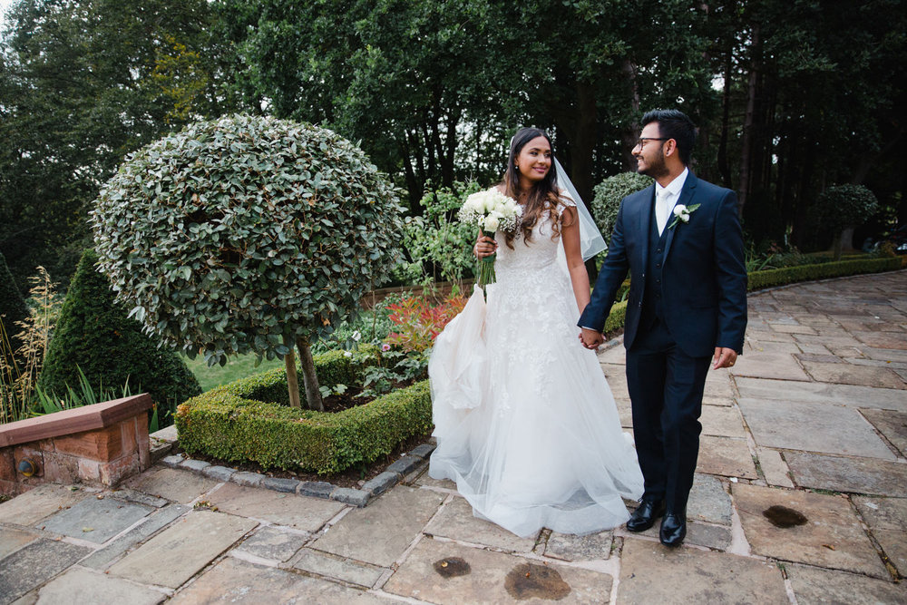 newlyweds in gardens of manor house as bride holds bouquet while looking at groom