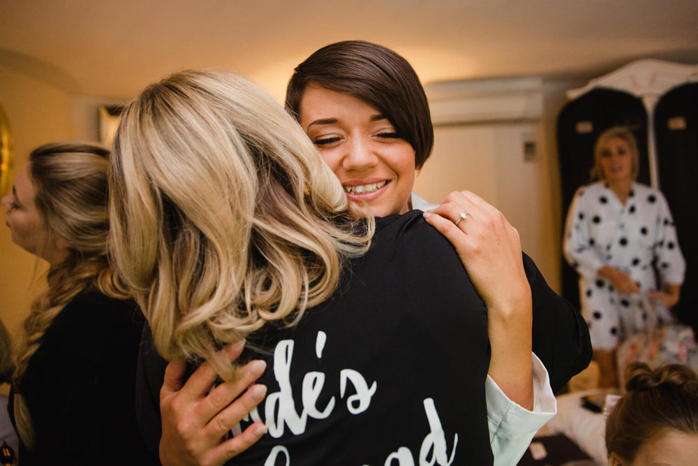 Copy of bride hugging bridesmaid sharing intimate relaxed moment before ceremony