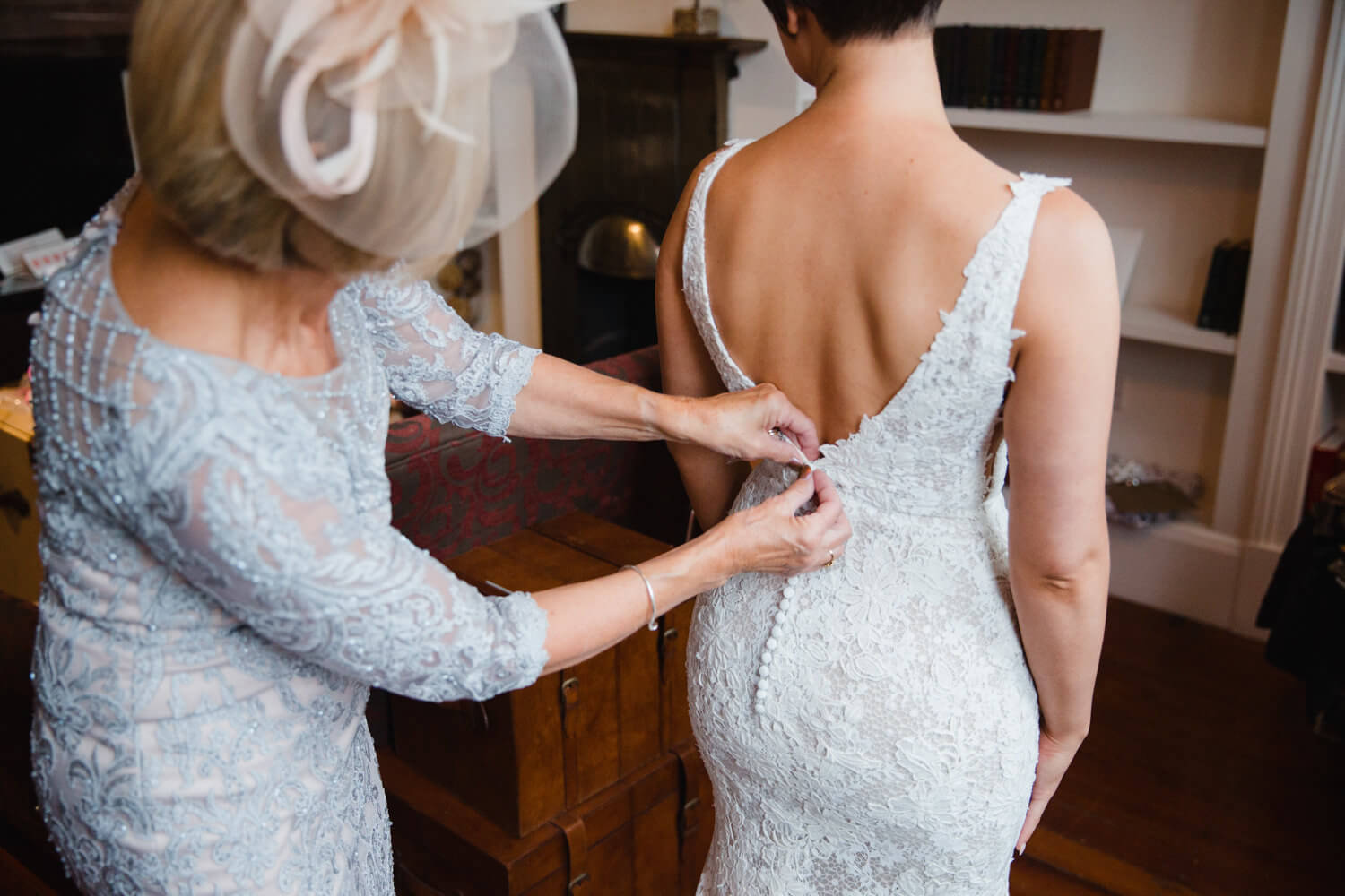 bride having wedding dress buttoned by mother