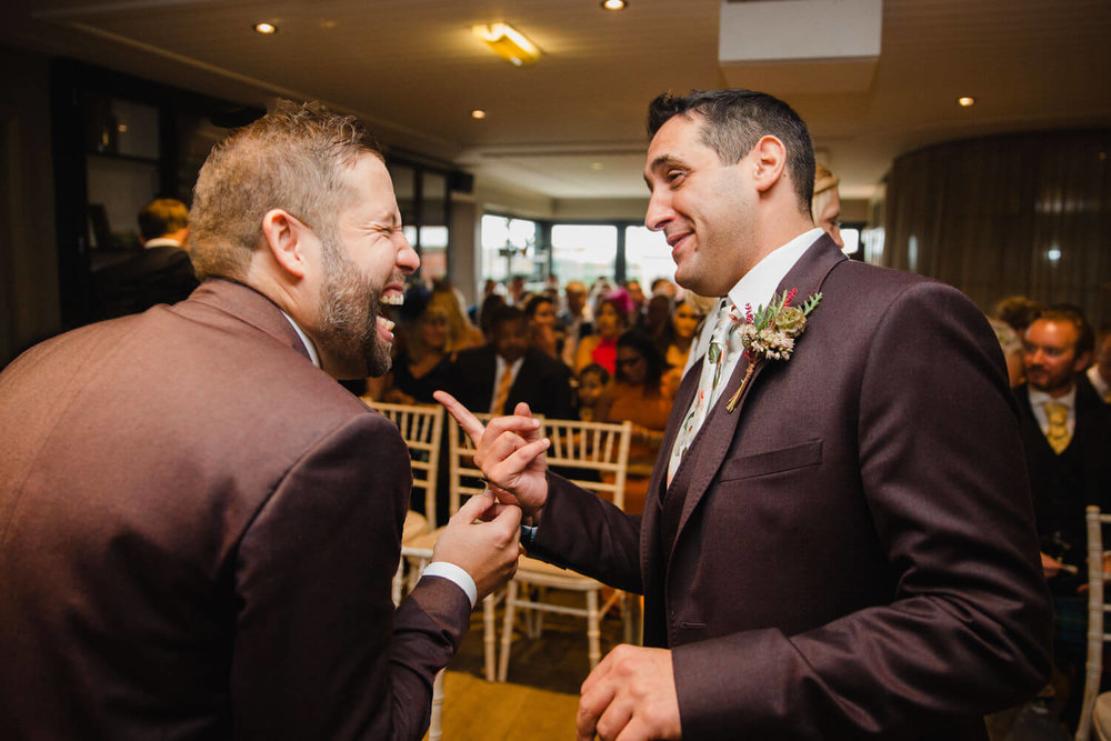 Copy of groom sharing joke with best man at the top of the aisle before wedding service