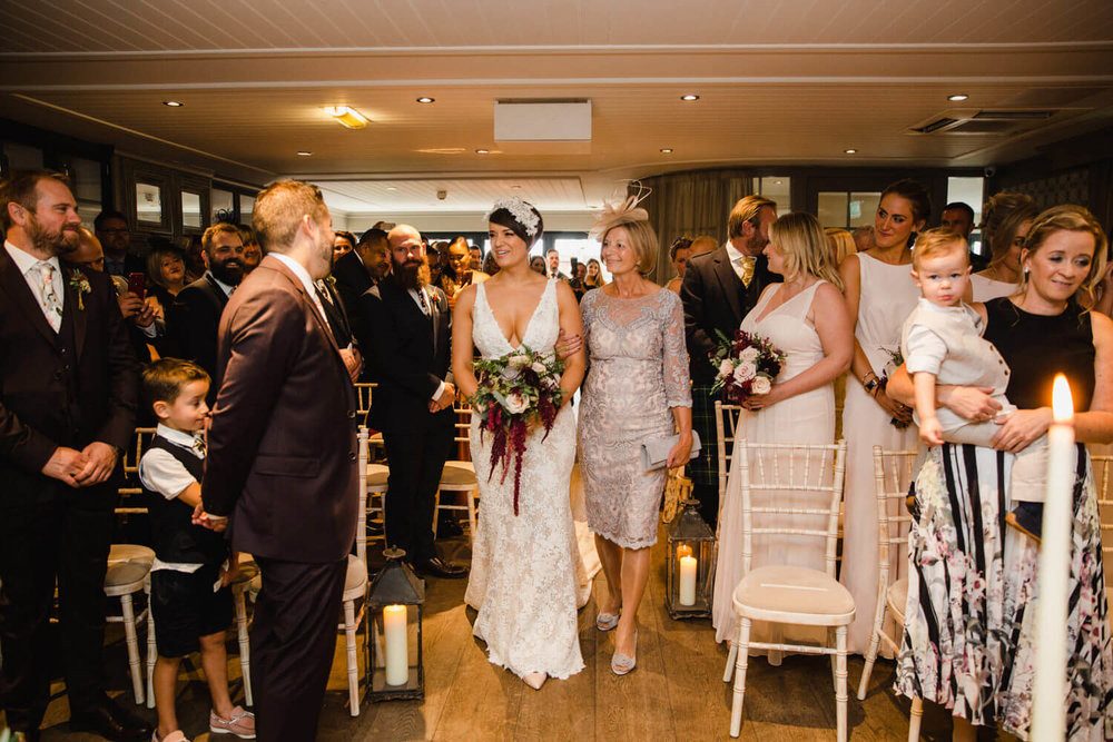 Copy of bride making her way down the aisle to ceremony processional as bridesmaids and groomsmen look on