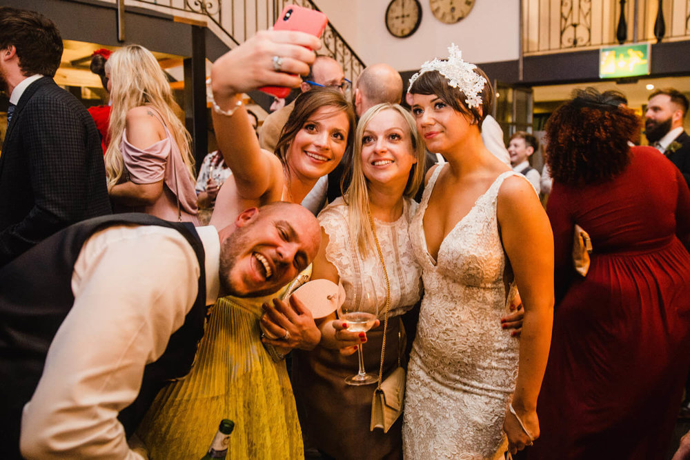 Copy of bride and guests enjoying camera phone photograph together on dance floor