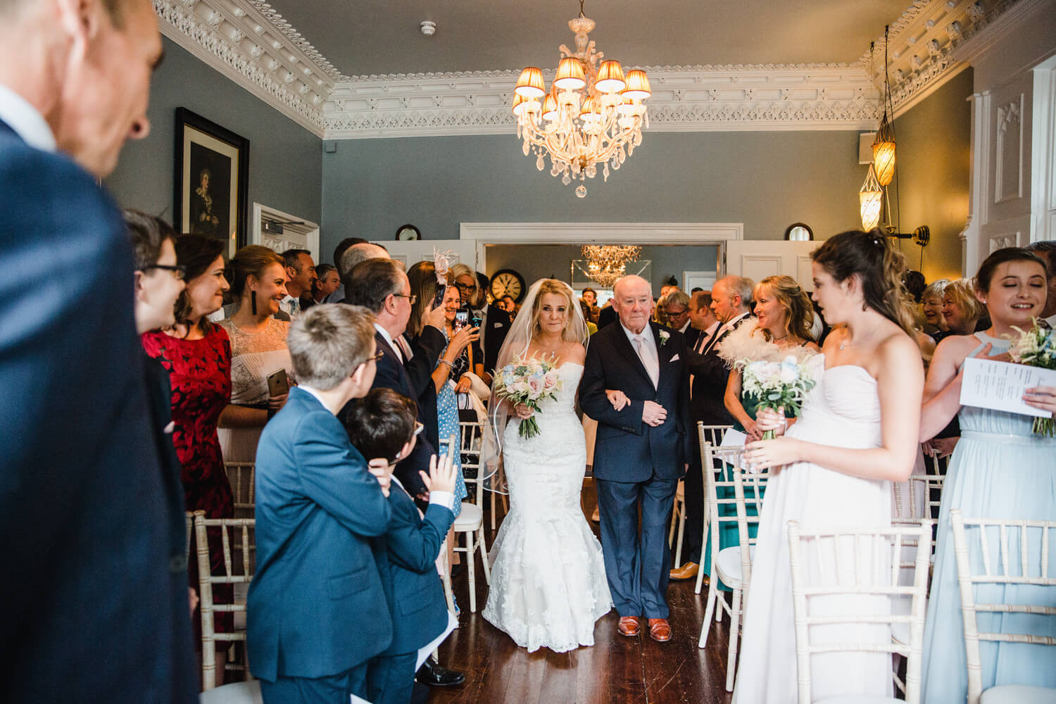 bride walking down aisle with father with groom in foreground and bridesmaids looking on