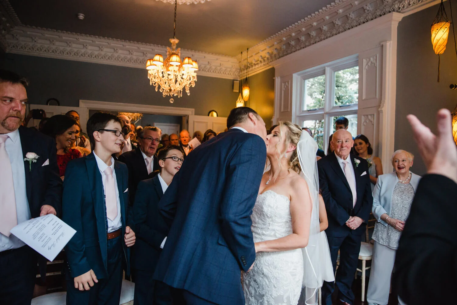 wide angle lens photograph of first kiss at didsbury house hotel as family and friends all celebrate