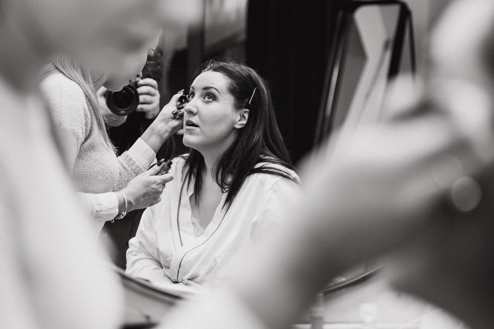 black and white low exposure photograph of bride having make-up applied in bridal suite