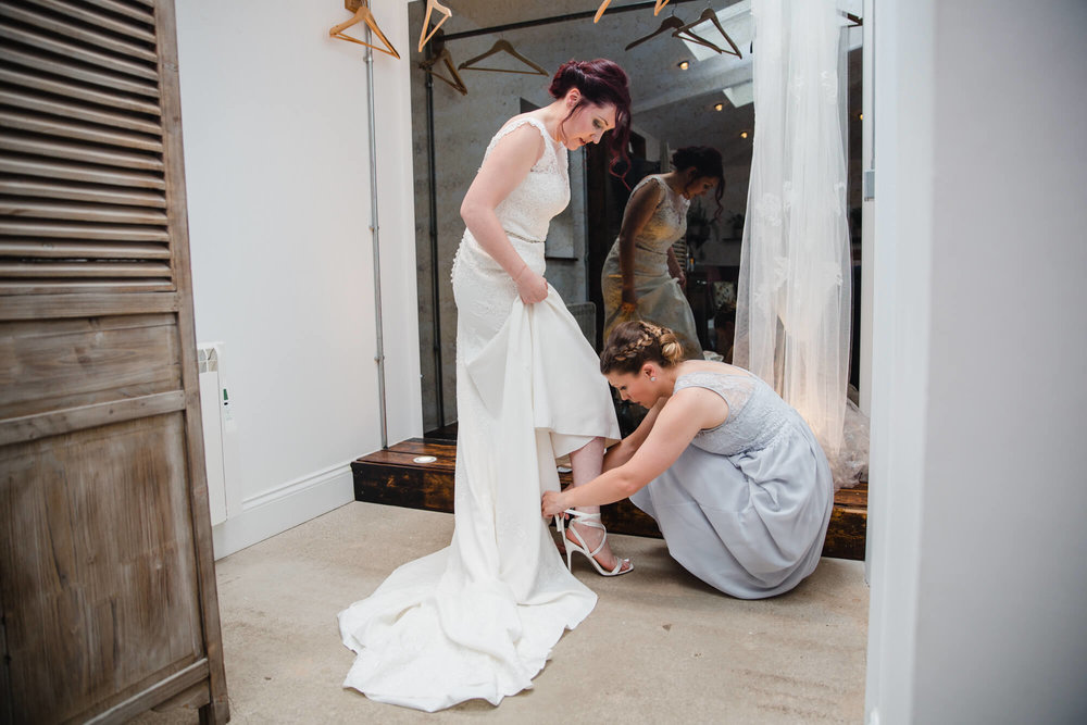 bridesmaid helping bride into wedding dress before ceremony begins