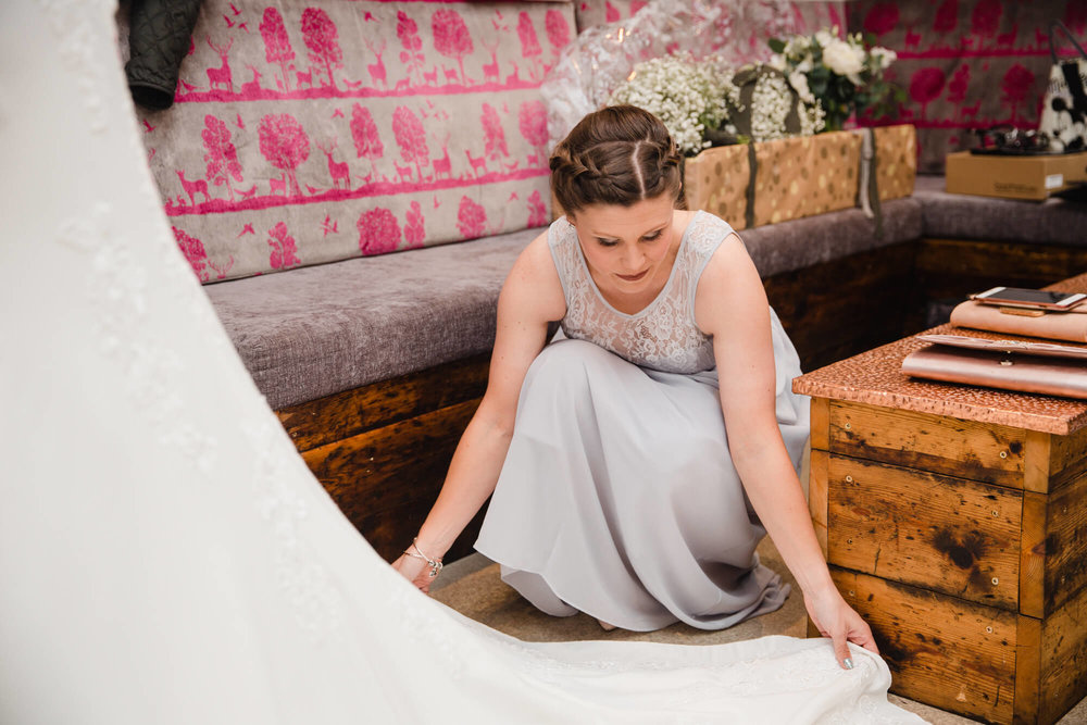 candid relaxed photograph of bridesmaid arranging wedding dress at owen house wedding barn