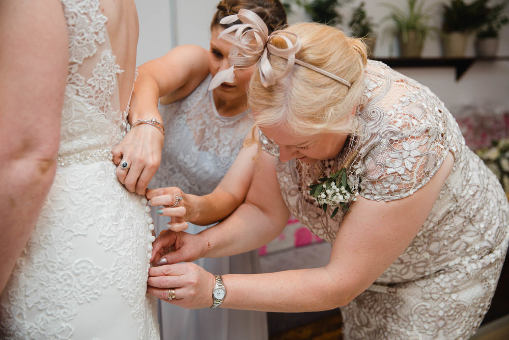 mother of bride helping bride fasten wedding dress