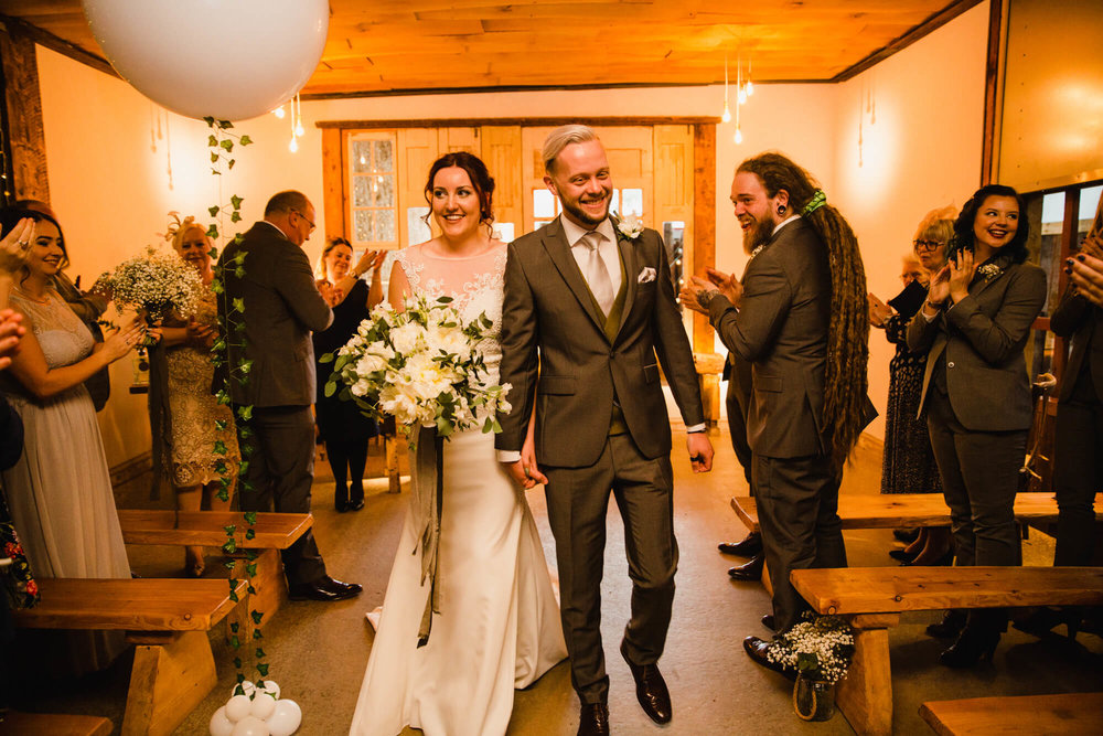 newlyweds walk down aisle while being applauded by wedding party