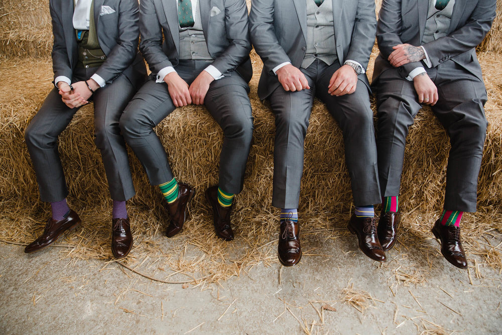 groomsmen posing on hay bale wearing striped coloured socks