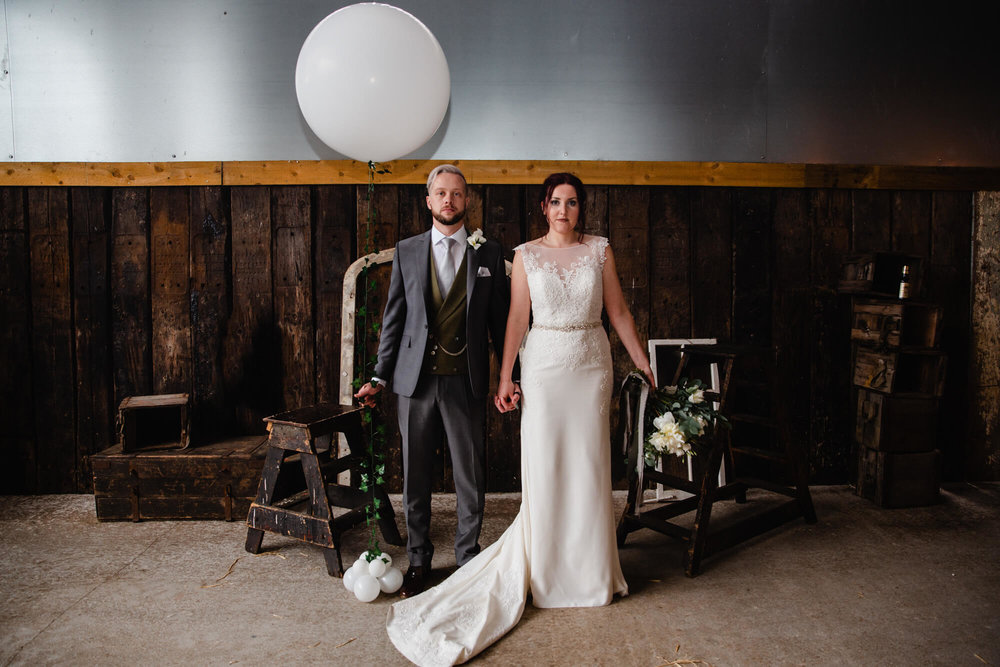 newlyweds pose looking at camera for portrait against barn wall backdrop