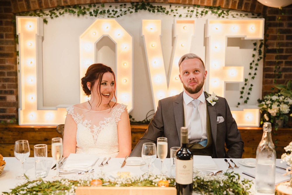 bride and groom sat at top table in foreground with LOVE letters in backdrop