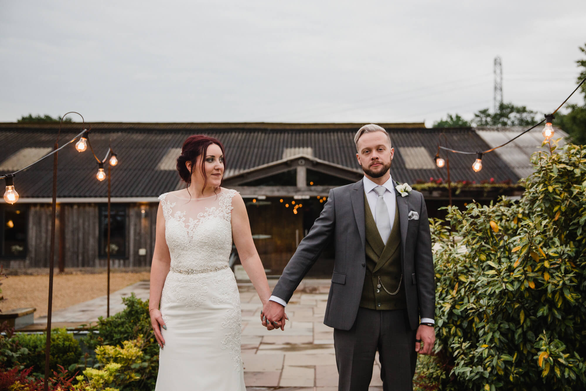 newlyweds hold hands while bride holds bouquet in front of barn doors at Owen House