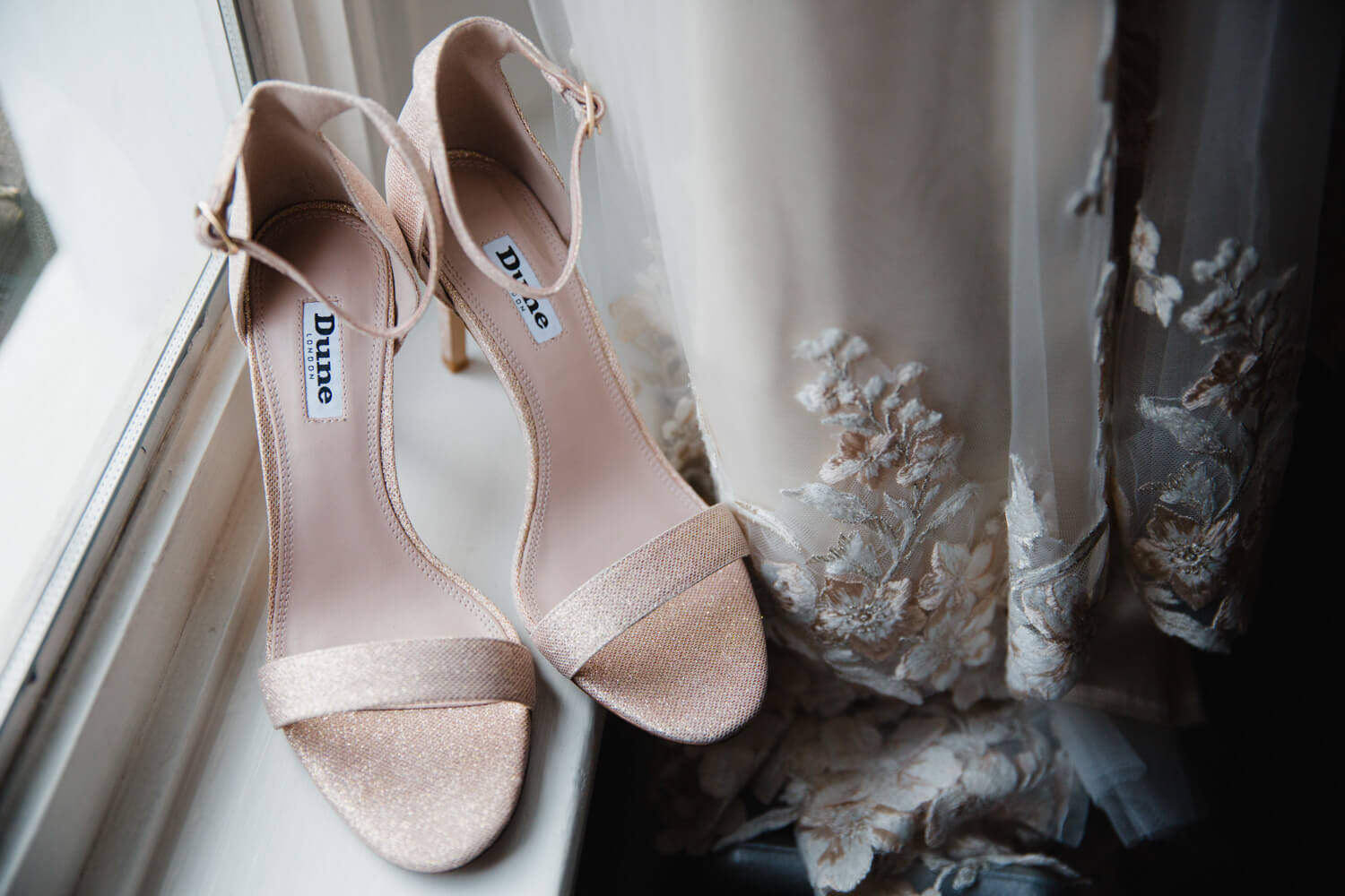 bridal wedding shoes on window alongside bridal gown