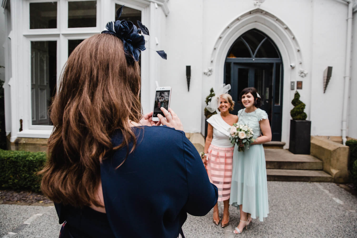 bridesmaid taking camera phone photograph of bridal party in front of Eleven Didsbury House