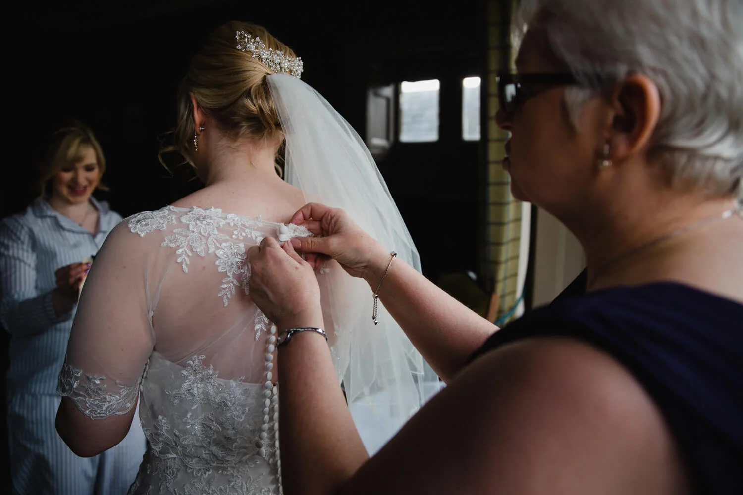 low light exposure photograph of mother of bride fastening wedding dress buttons