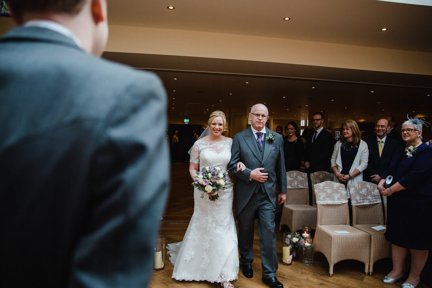 bride and father linking arms while smiling at groom in foreground