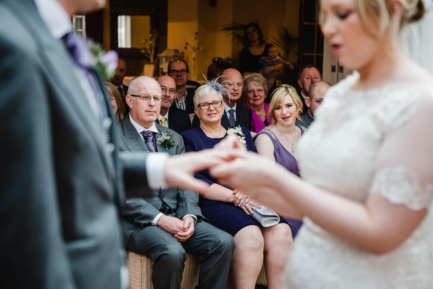 Mother of Bride smiling while newlyweds exchange rings at Mitton Hall